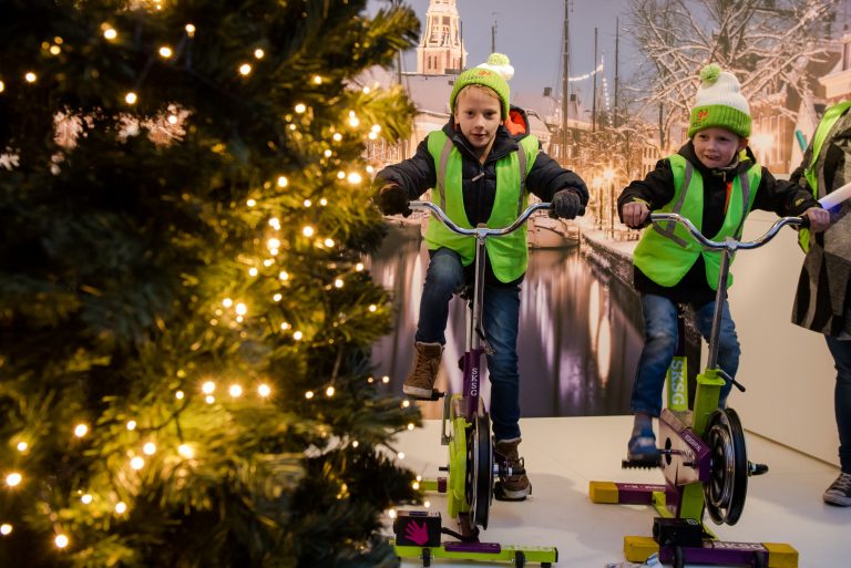 Kinderen ontsteken lampjes in kerstboom op powerbikes